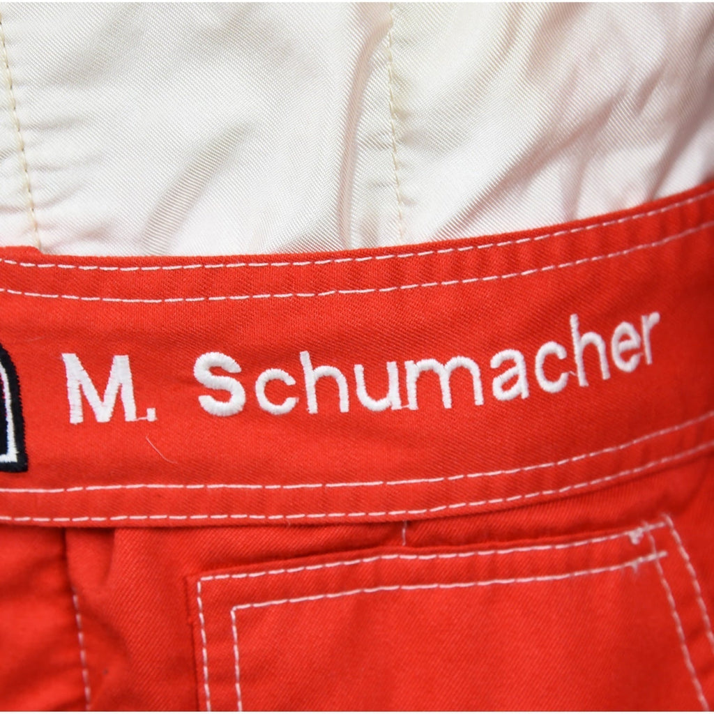 Close-up of Schumacher’s 1997 F1 race suit, displaying detailed stitching and rich red fabric, with sponsor logos highlighting his drive during the 1997 season.