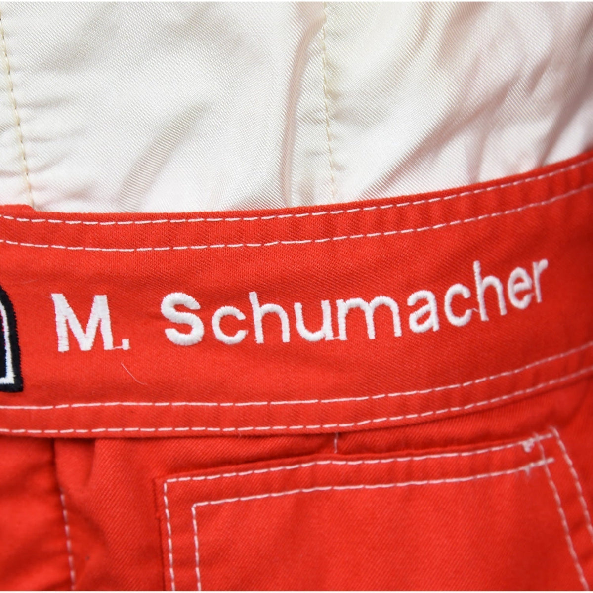 Close-up of Schumacher’s 1997 F1 race suit, displaying detailed stitching and rich red fabric, with sponsor logos highlighting his drive during the 1997 season.