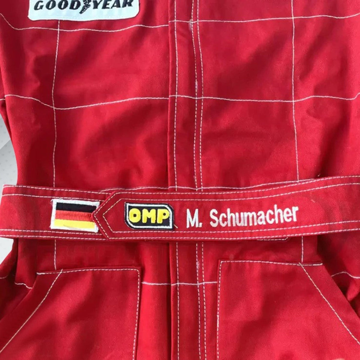 Close-up of Schumacher’s 1996 F1 suit, featuring the detailed stitching, Ferrari red color, and early sponsor branding from his debut season