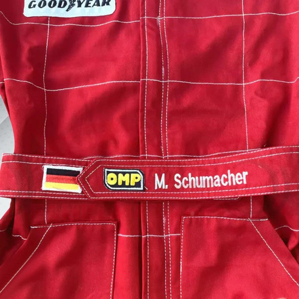 Close-up of Schumacher’s 1996 F1 suit, featuring the detailed stitching, Ferrari red color, and early sponsor branding from his debut season