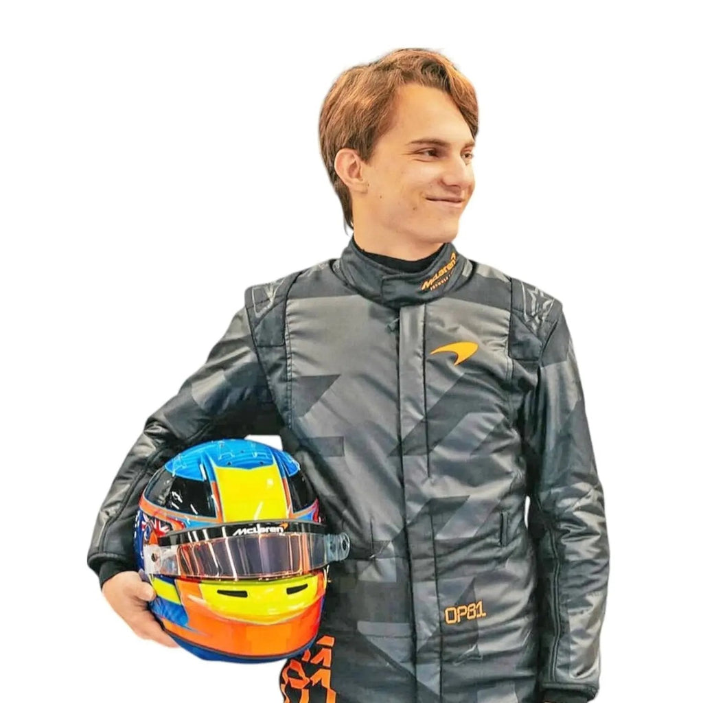 Close-up of  Piastri holding custom-designed helmets — Piastri with a high-gloss blue-yellow-red helmet—contrasting the matte black suit.